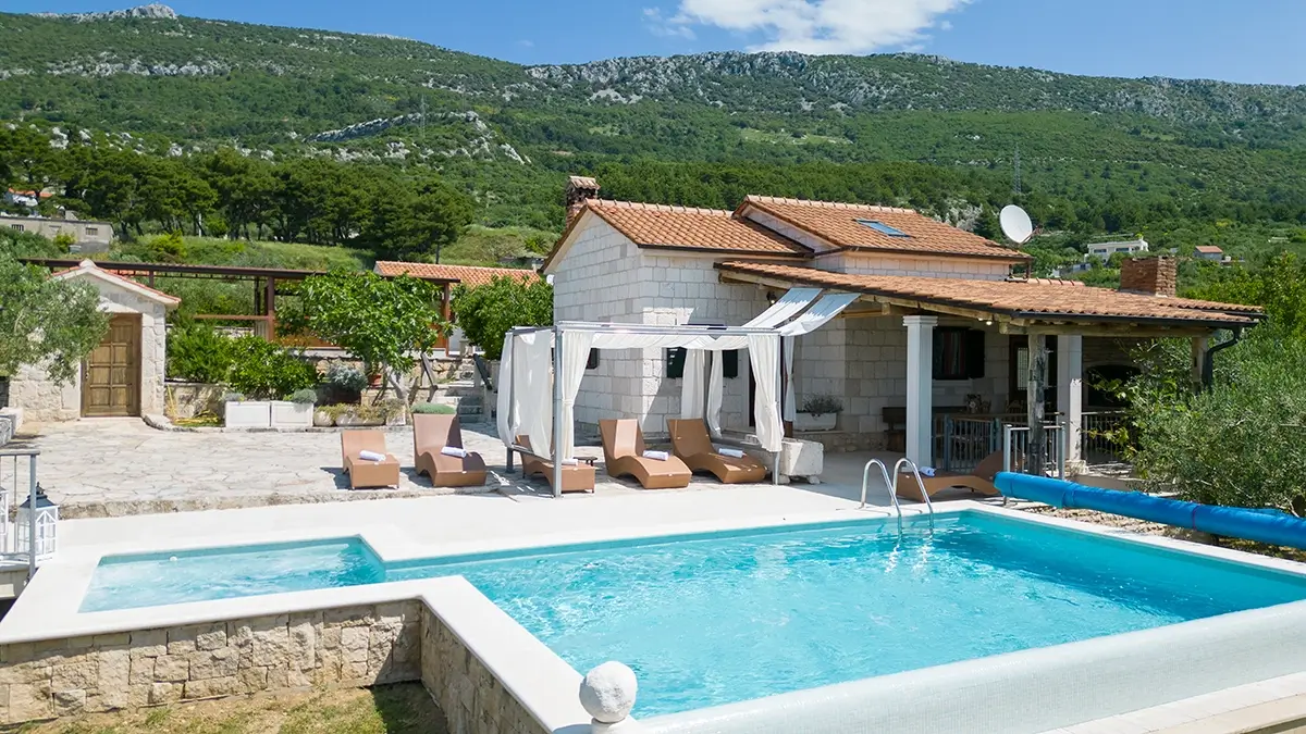 View of the villa from the outside, with a swimming pool and lounge chairs, at the foot of the mountain.